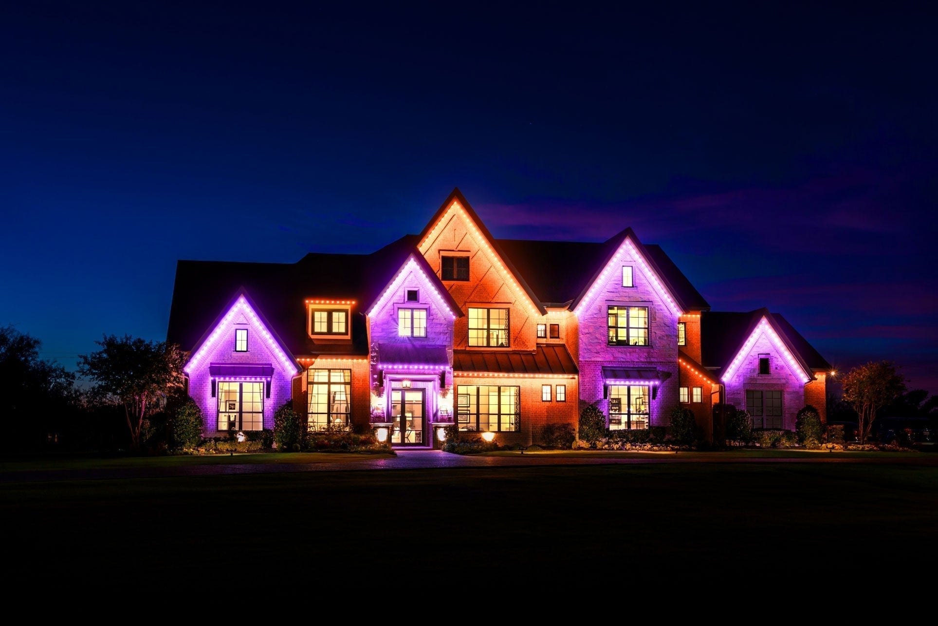 Large home at night with purple and orange roofline lights across multiple gables.