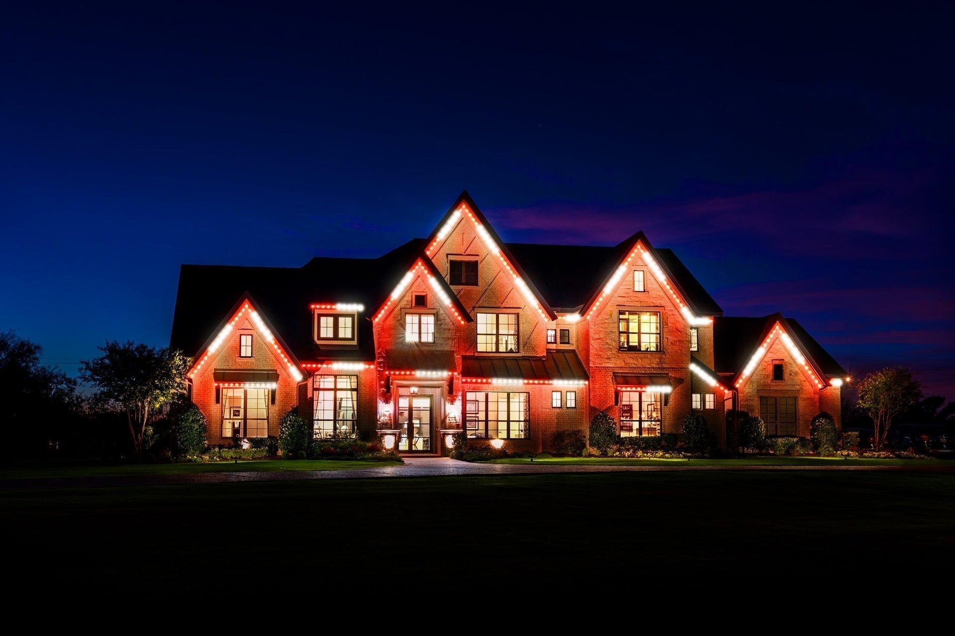 Large brick home with permanent roofline lights in classic red and white.